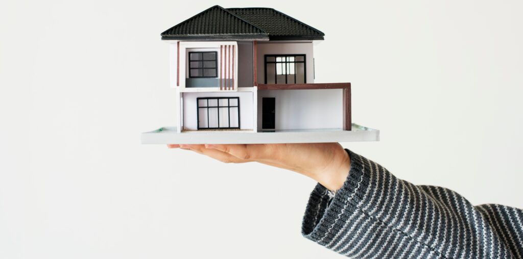 A hand holding a miniature house, symbolizing property investment and ownership.